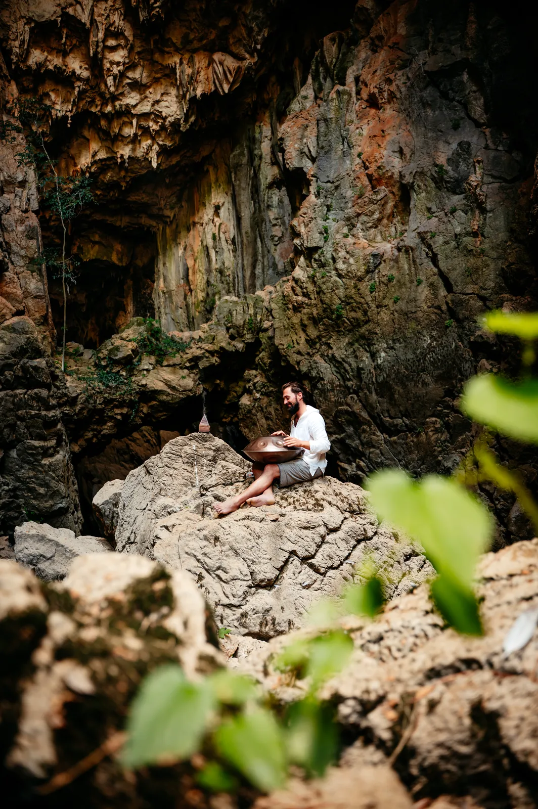 Simon plays the handpan on a rock in front of a cave