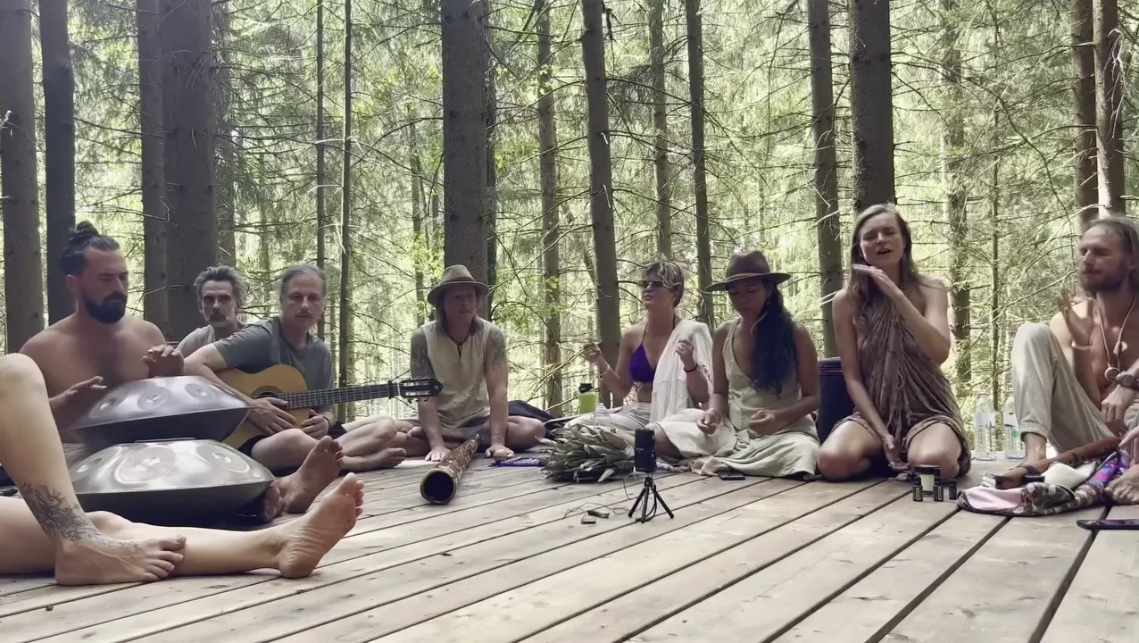 Musicians sit in a circle on a wooden platform in the forest