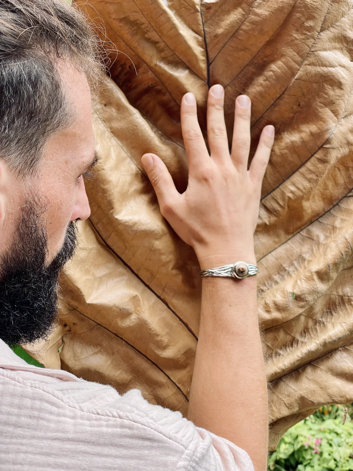 Simon's hand on a large dried leaf, wearing an MGK bracelet