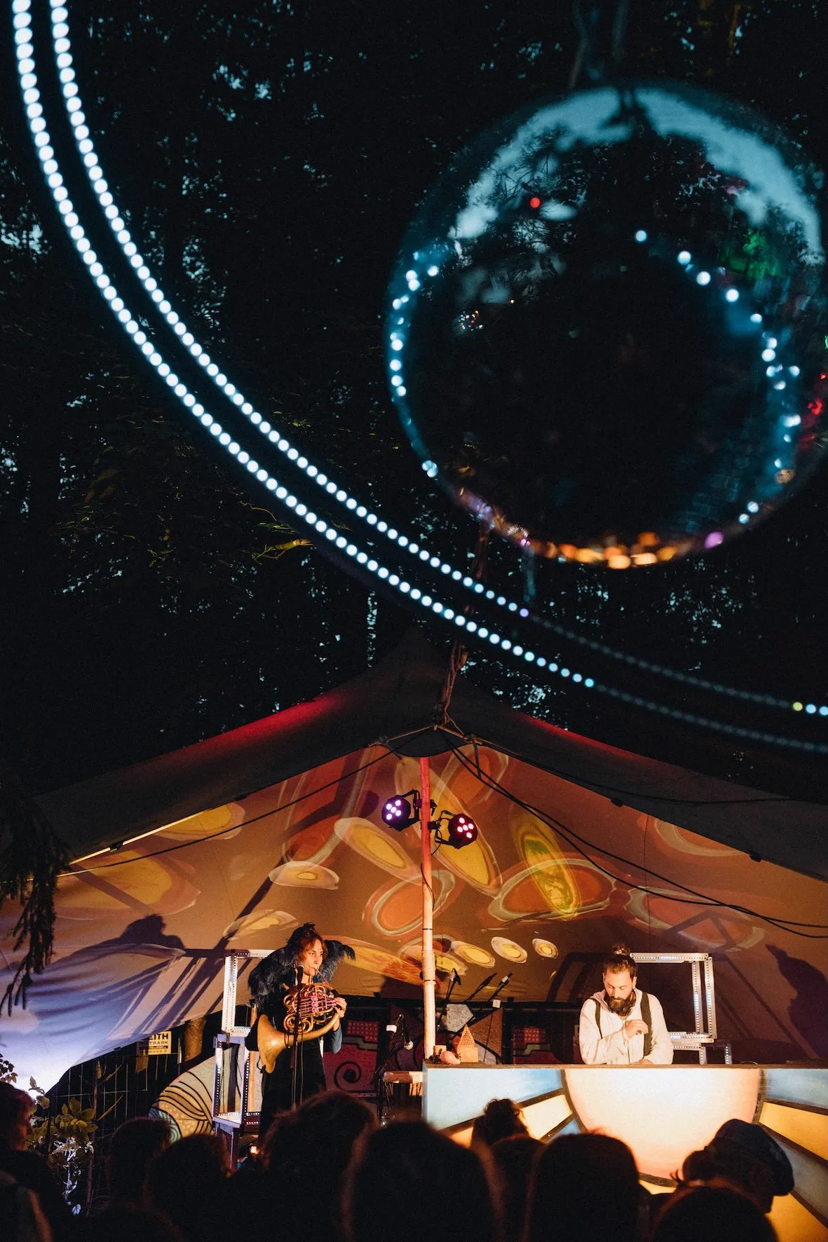 A festival tent at night under a mirror ball and strings of light