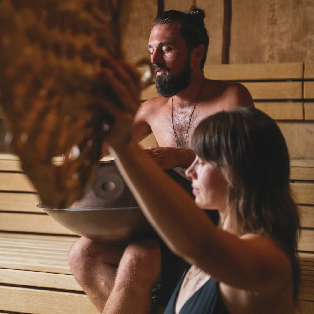 Simon holds a handpan in the sauna while a guest fans the steam